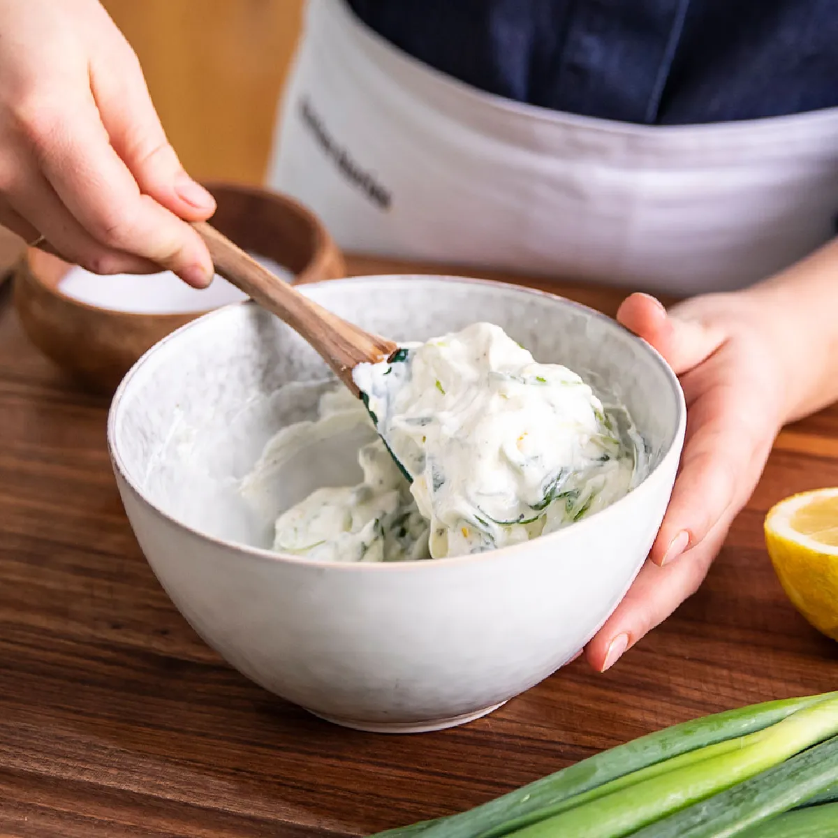 Mani mescolando ingredienti in una ciotola, con un limone e cipolle verdi su una superficie di legno