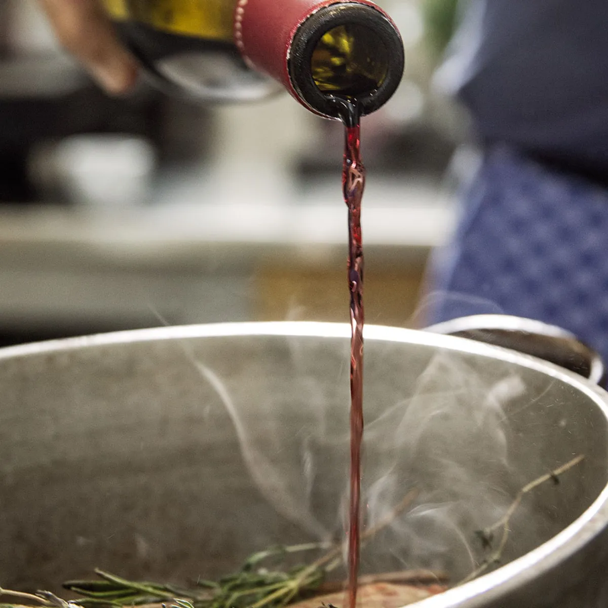 Vino rosso versato in una pentola fumante con delle erbe aromatiche, mentre cuoce in una cucina