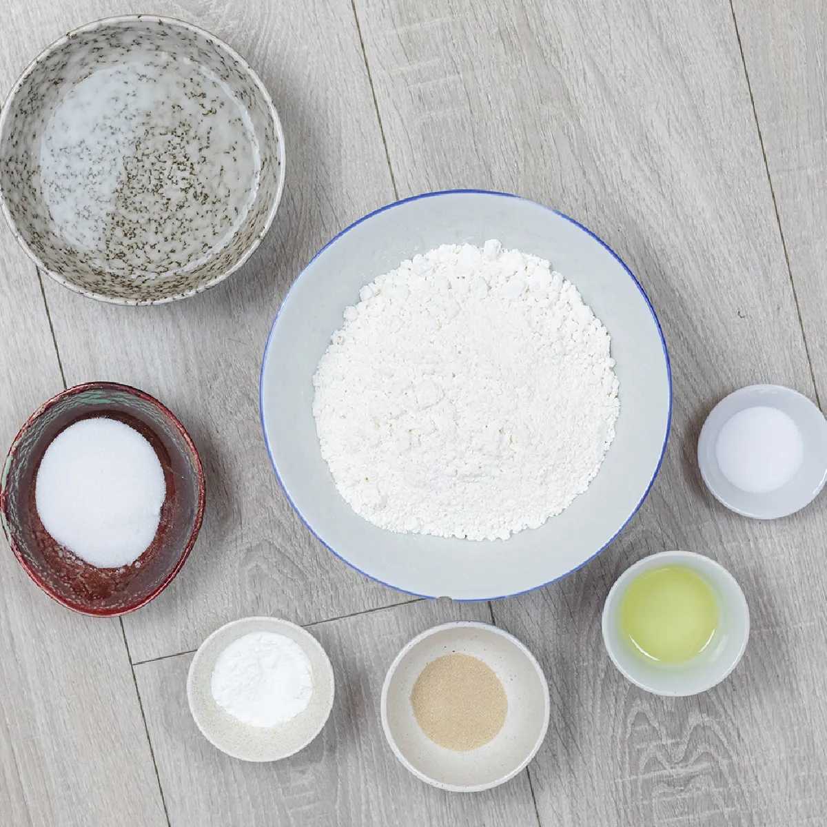 Vista superiore dei piatti con harina, acqua, levadura, aceto e sale disposti su una superficie di legno per gli ingredienti della replica