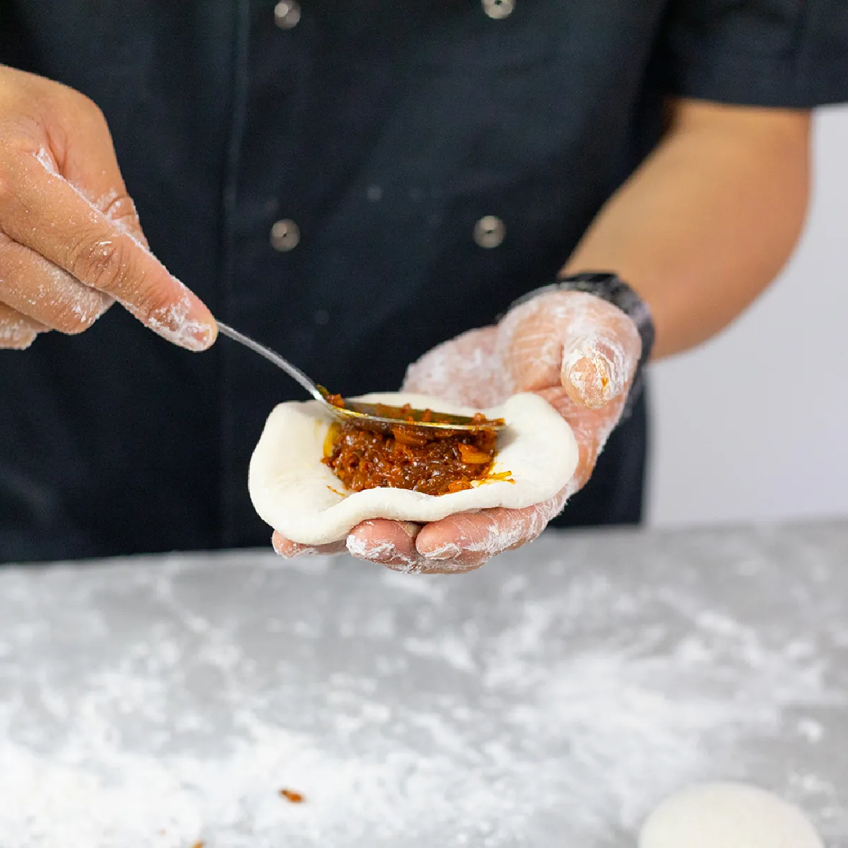 Farcitura e modellatura dell'impasto per formare panini con ripieno di maiale e kimchi su un piano di lavoro della cucina