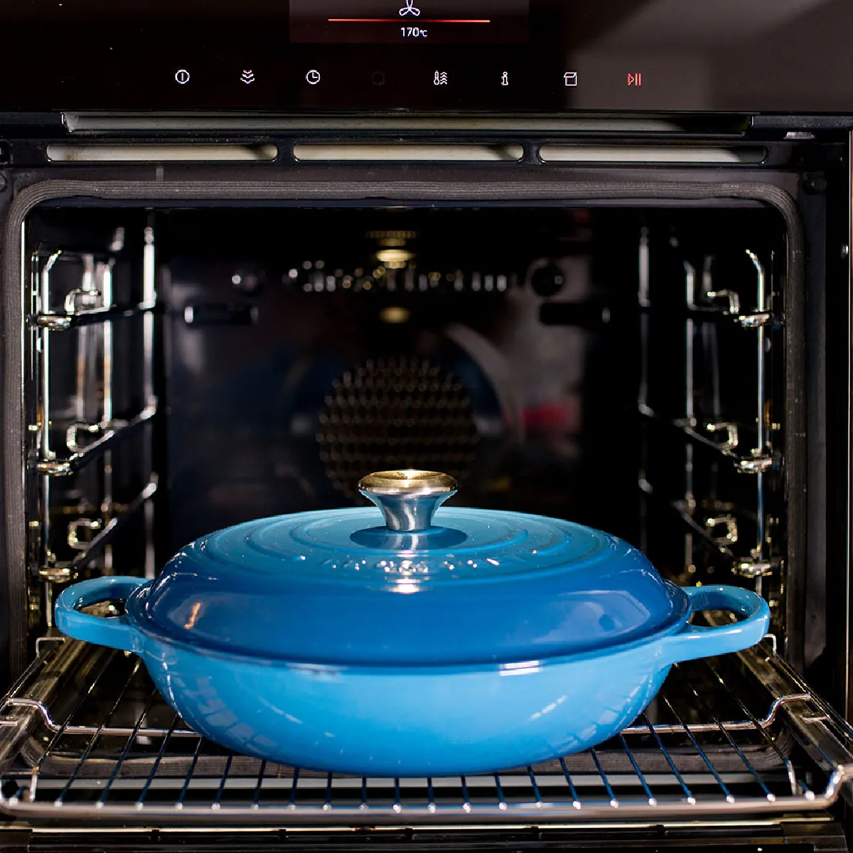 Pentola in ghisa blu con coperchio all'interno di un forno aperto incorporato in una cucina moderna.