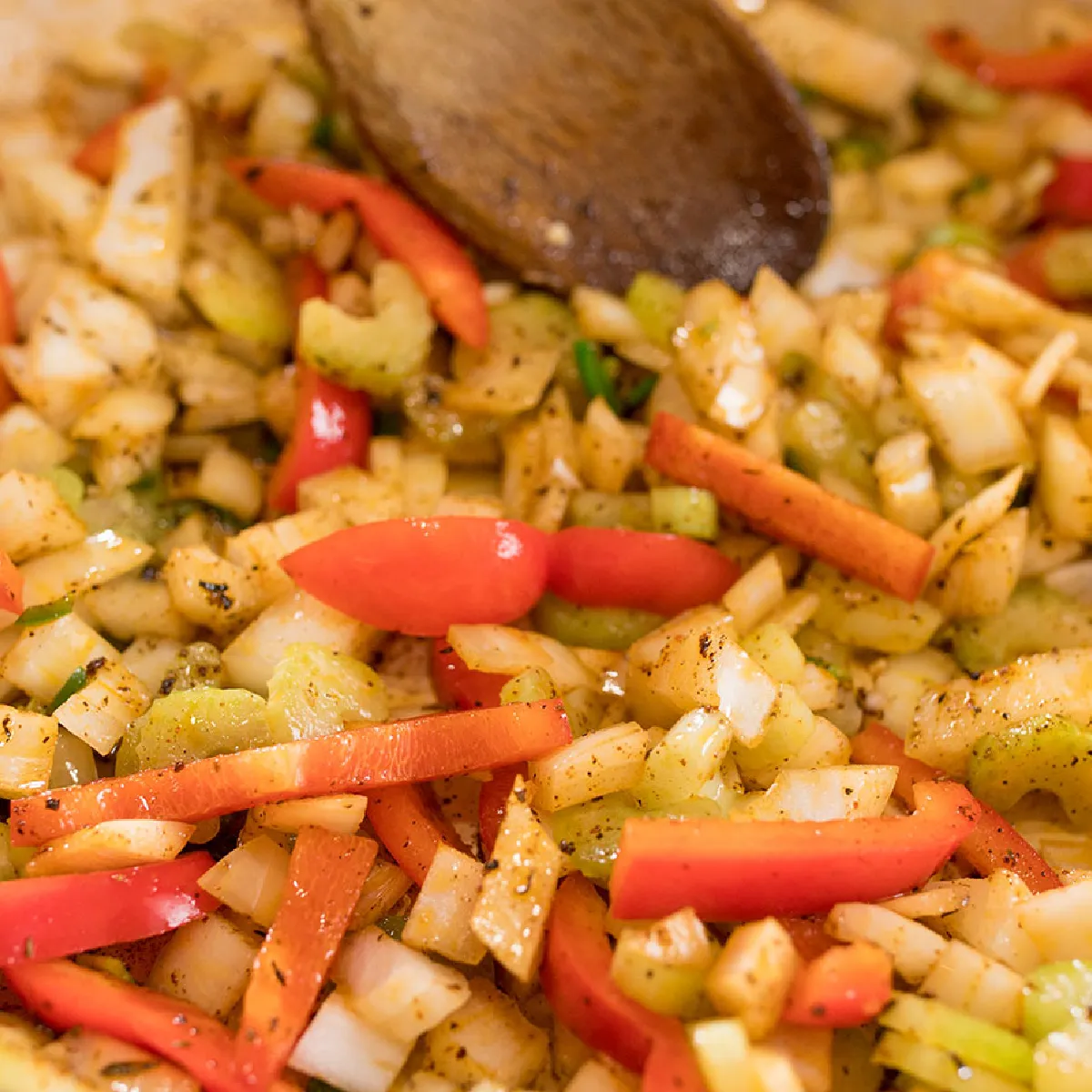 Un mix colorato di cipolle tritate, peperoni rossi, sedano e carote saltate in padella con erbe e spezie.