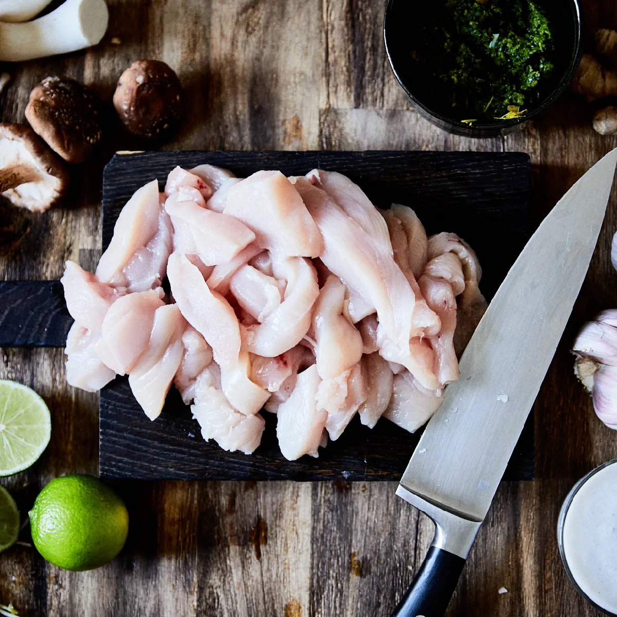 Pollo crudo, funghi, aglio, lime, coltello su tavola di legno - ingredienti di cottura e utensili.