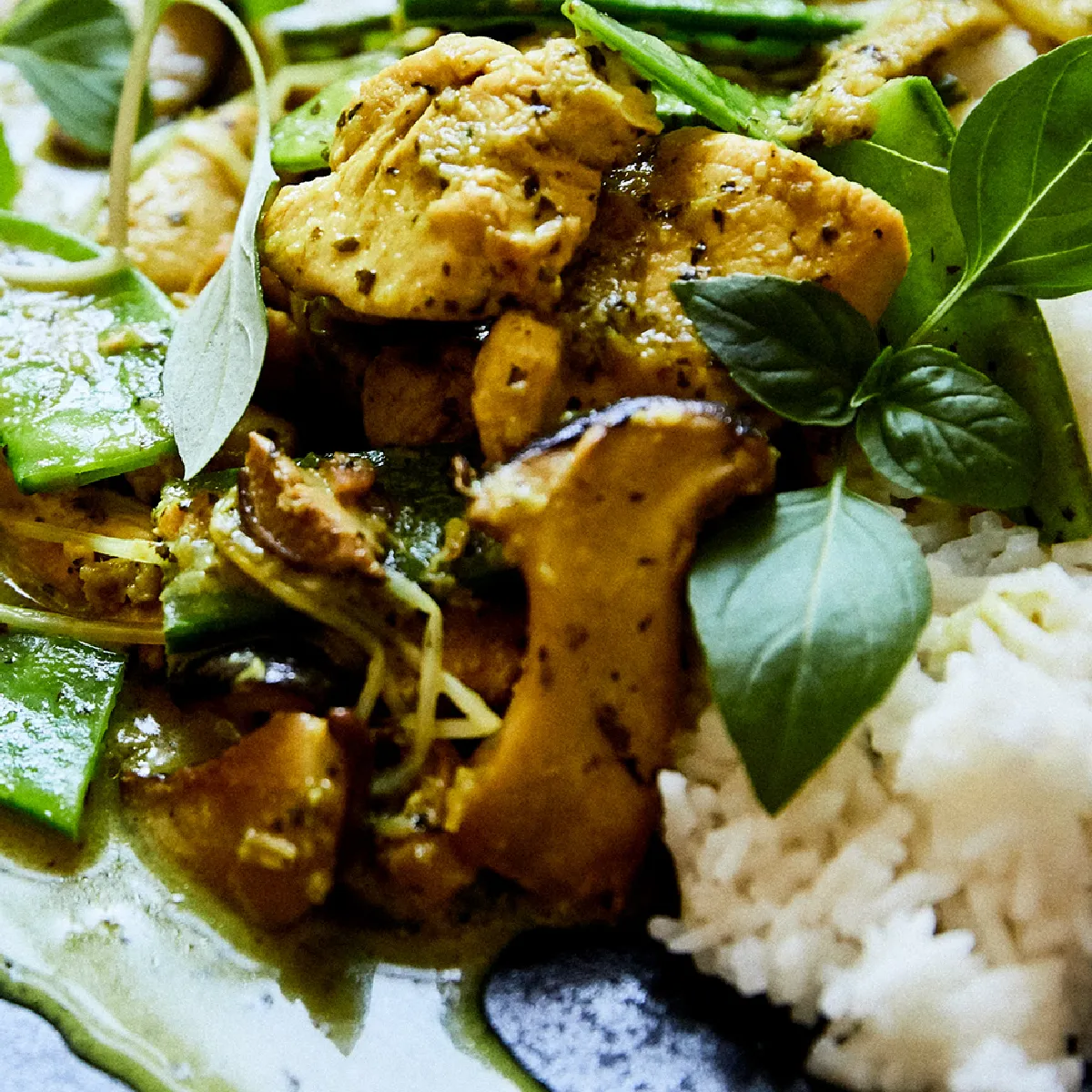 Curry verde thailandese con pezzi di pollo, verdure e foglie di basilico su un piatto con riso bianco