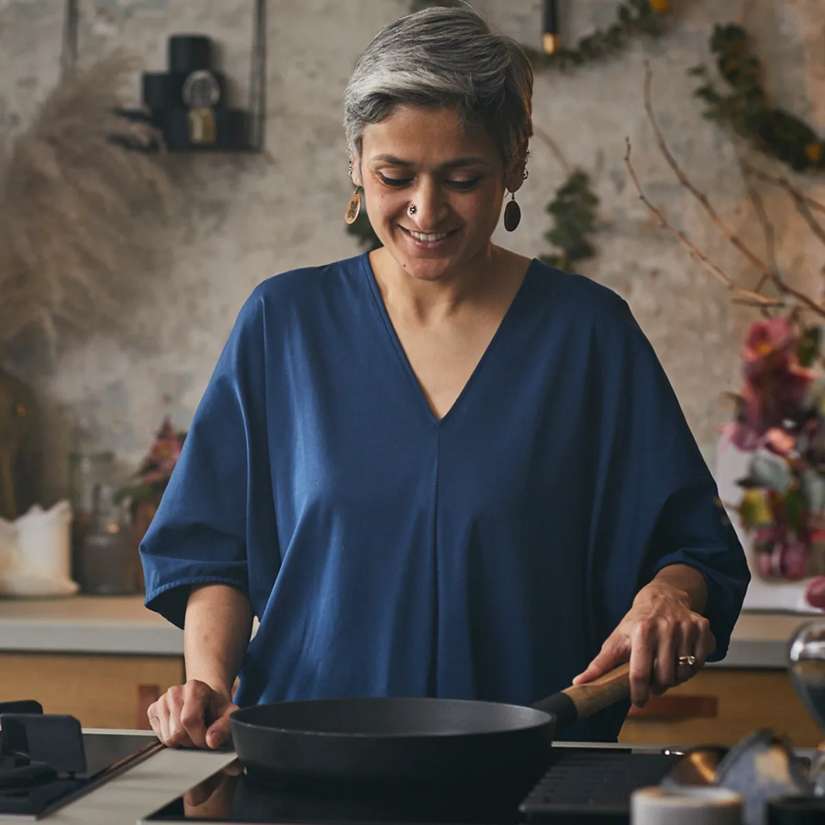 Persona con maglia blu in cucina moderna davanti a fornello e padella