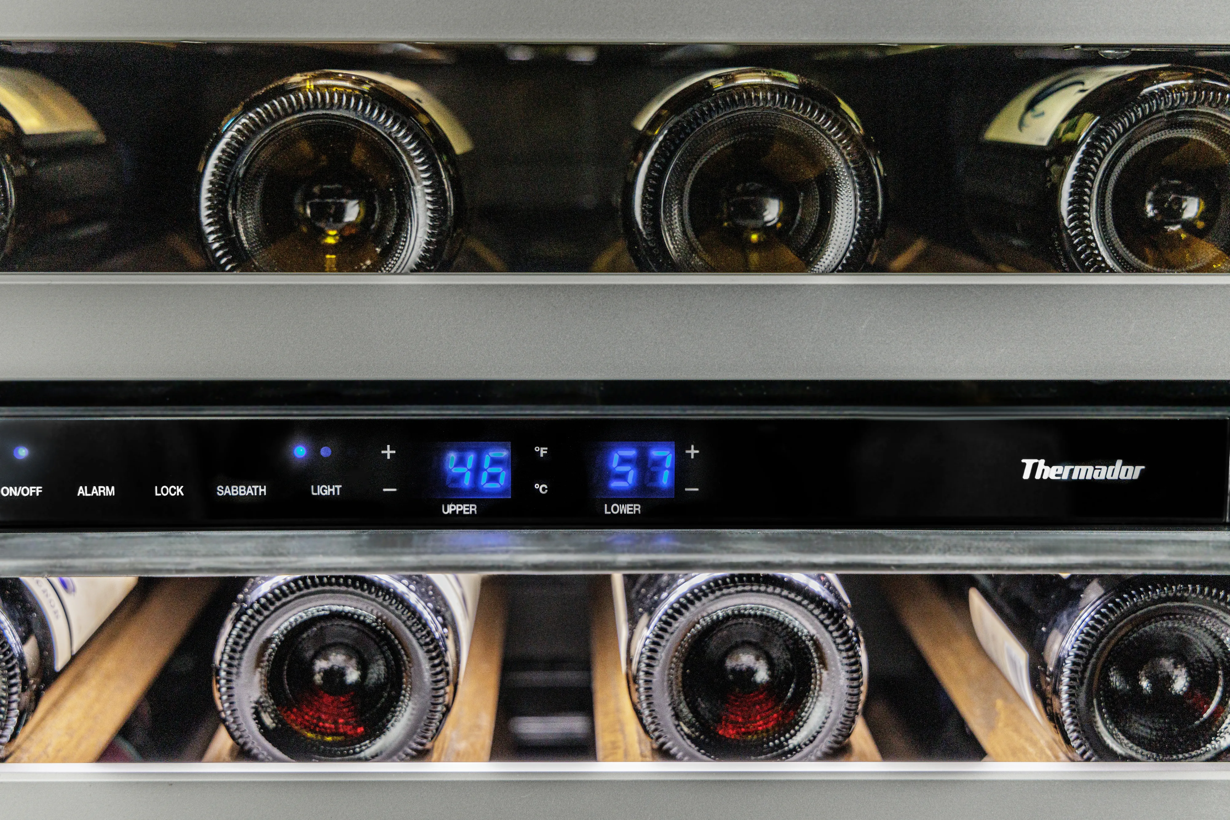 Close-up of a sleek black wine cooler displaying temperature controls and illuminated bottles inside.