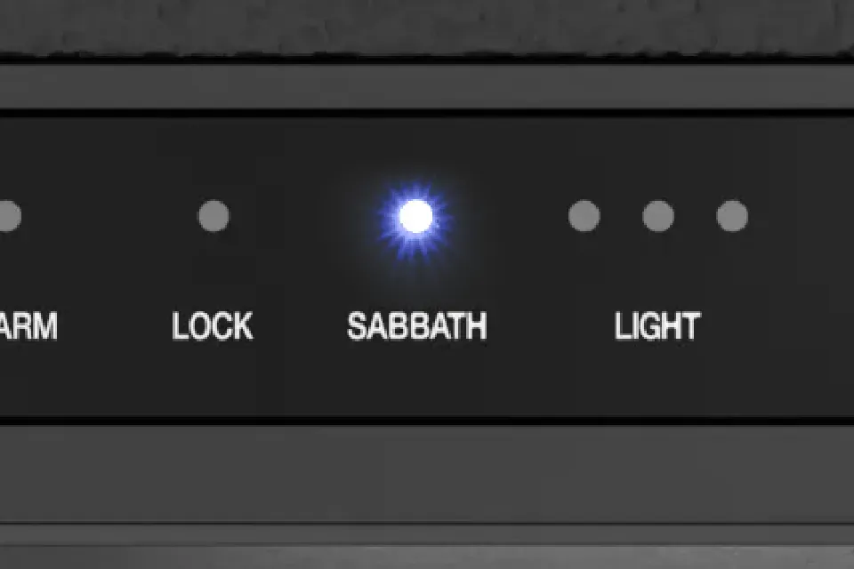 Close-up of a black appliance control panel with small circular indicator lights above the labels "ARM," "LOCK," "SABBATH," and "LIGHT"; the "SABBATH" indicator is lit with a bright blue LED.