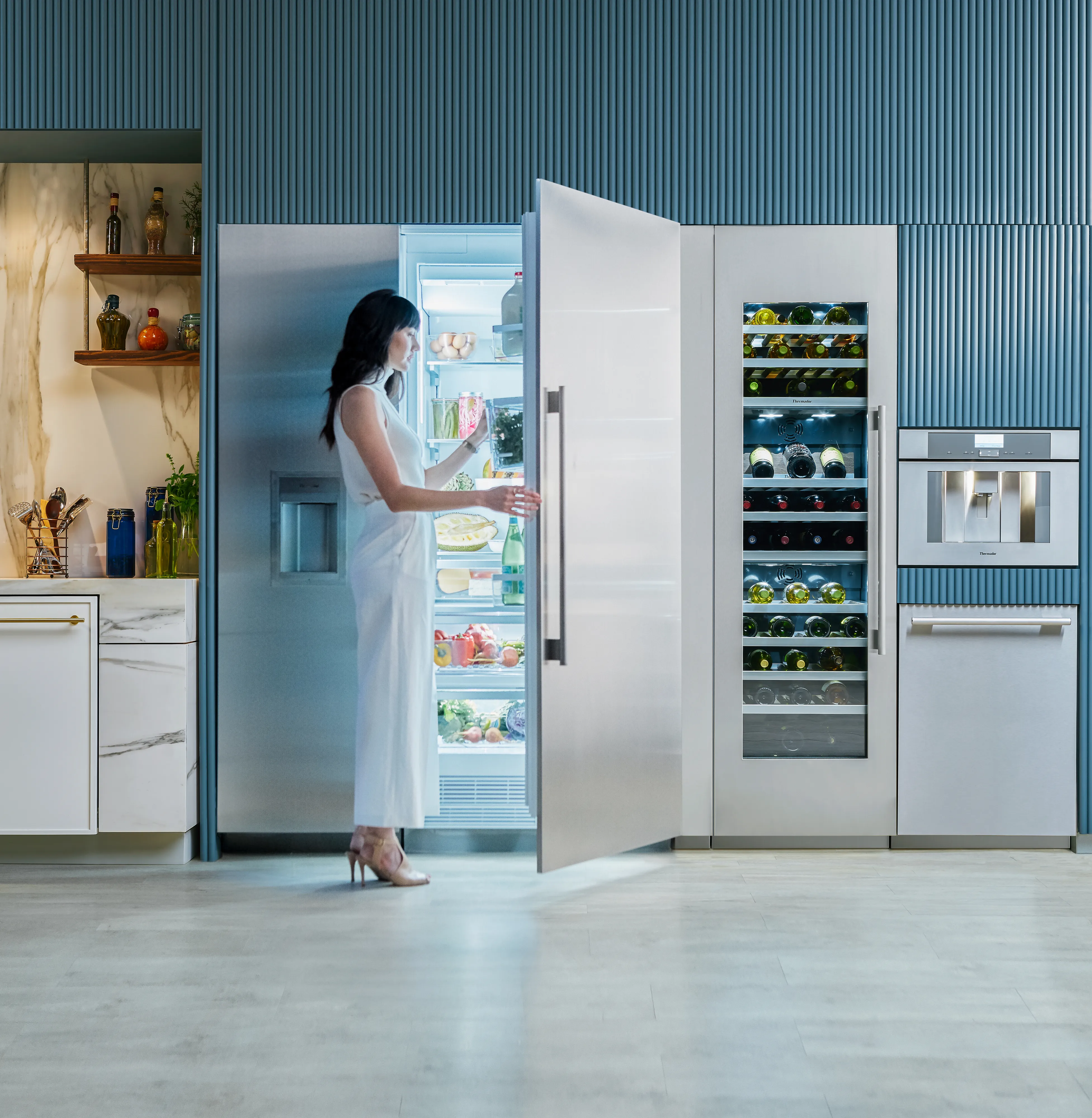 A person in a white dress stands in a modern kitchen with blue textured cabinetry