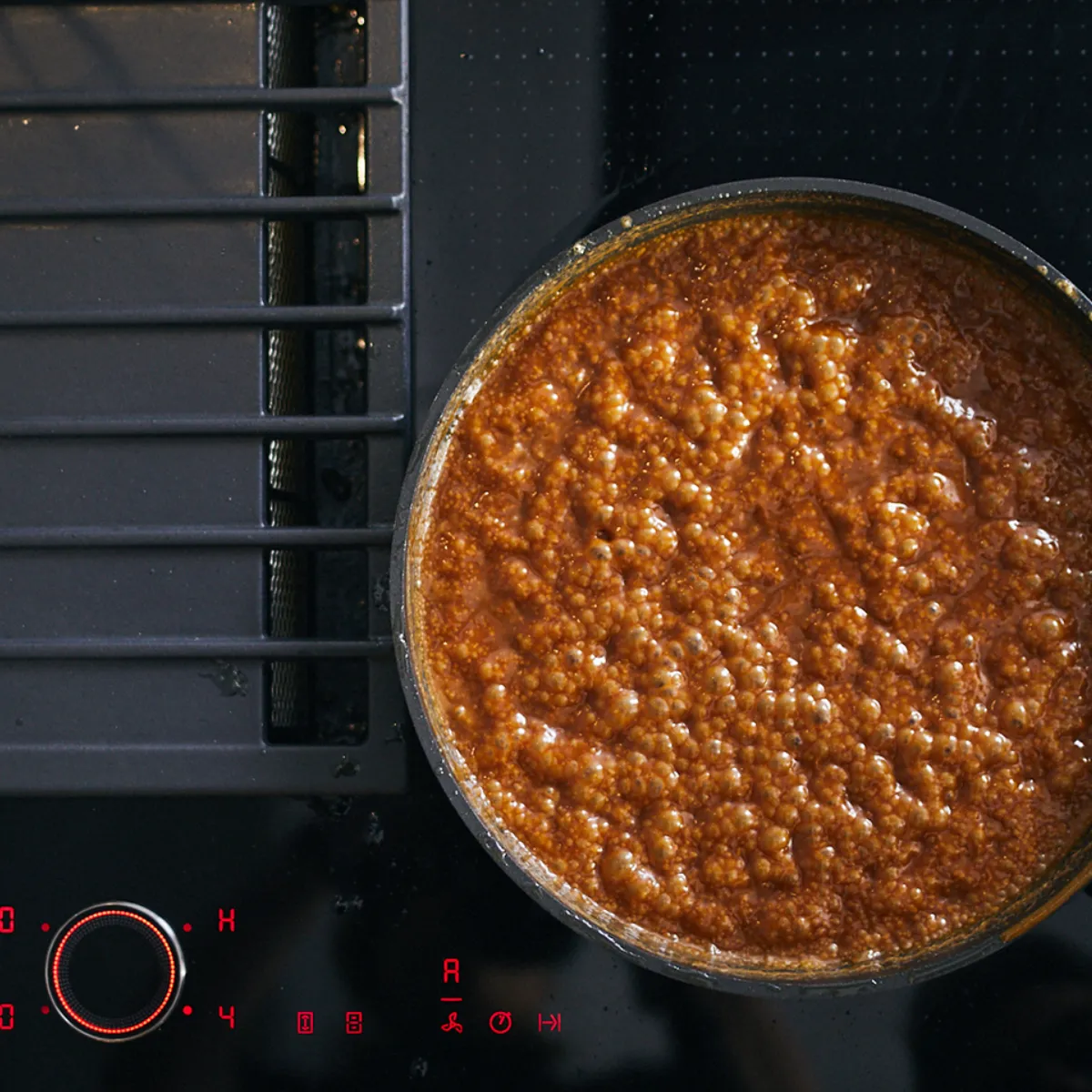 Σάλτσα που σιγοβράζει σε τηγάνι σε μαύρη κουζίνα. 