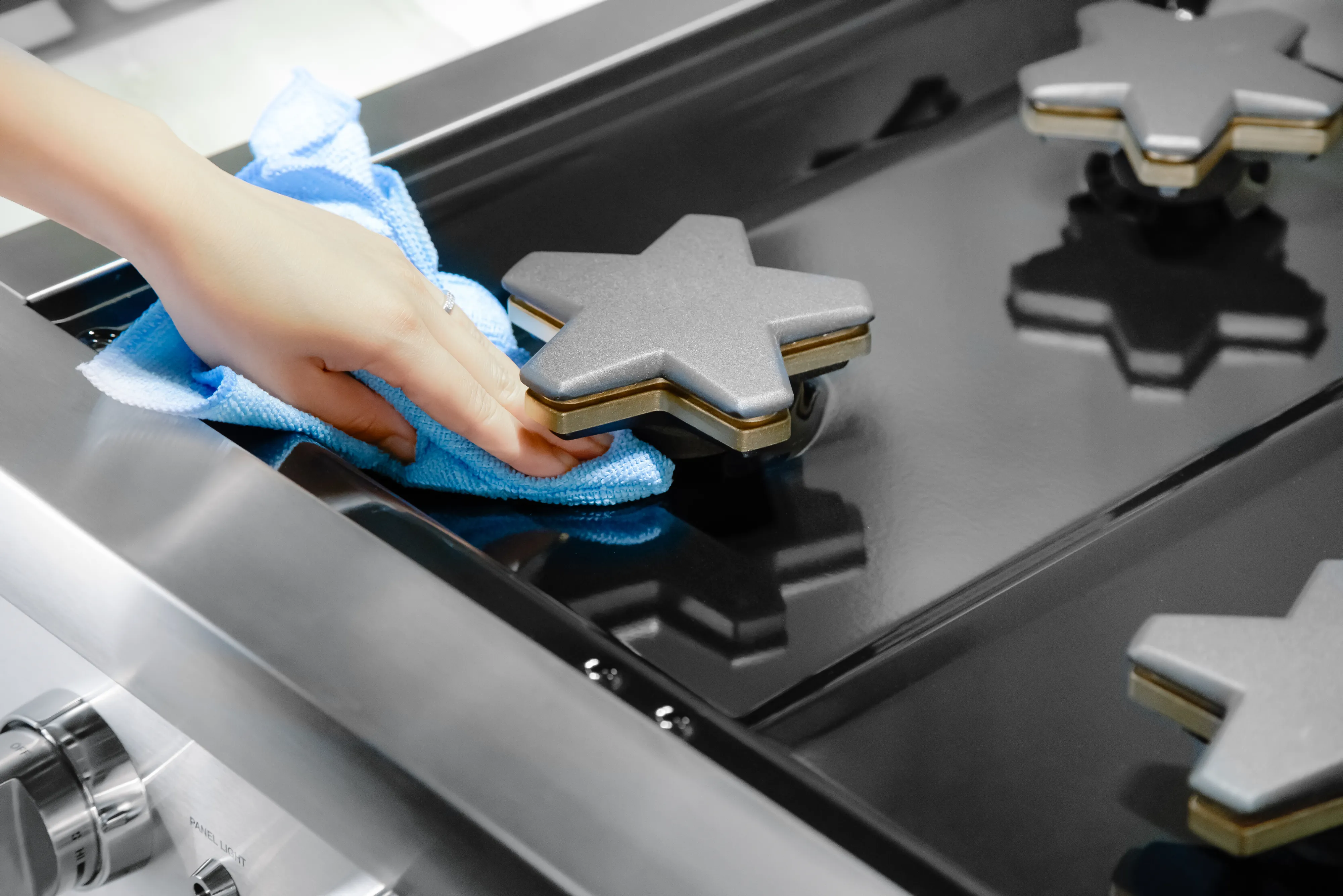 Hand cleaning a black gas stove with a blue cloth, focusing on a star-shaped burner cover.