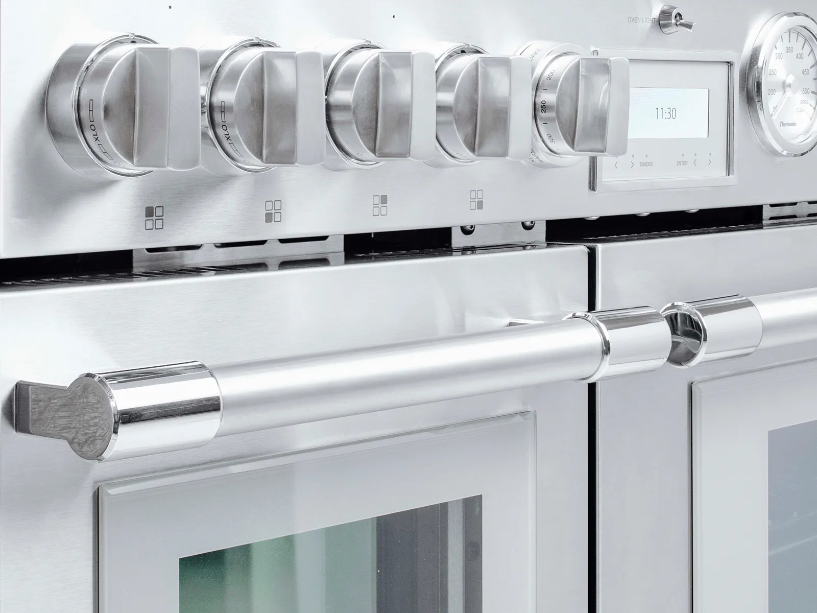 Close-up of a modern stainless steel oven with control knobs, digital display, and large sturdy handles.