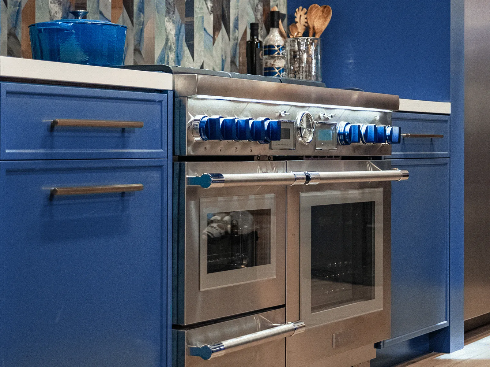 Modern kitchen with blue cabinetry and a stainless steel double oven featuring blue knobs and handles.