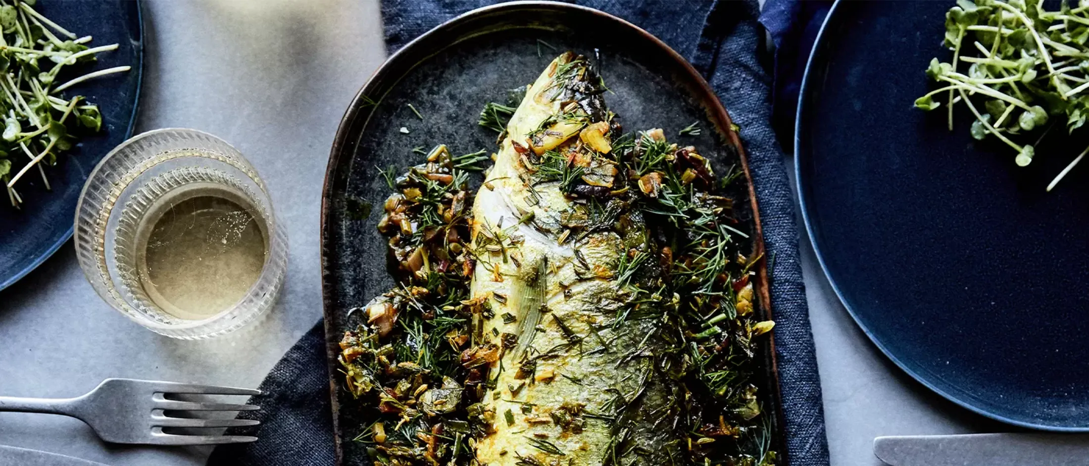 Filetto di pesce al forno con crosta di erbe, servito su piatto scuro con piatti laterali.
