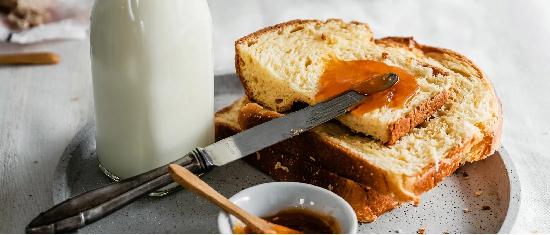 Fette di pane con marmellata d'arancia e un coltello da burro su un piatto, accompagnate da una bottiglia di latte e da una piccola ciotola di marmellata.