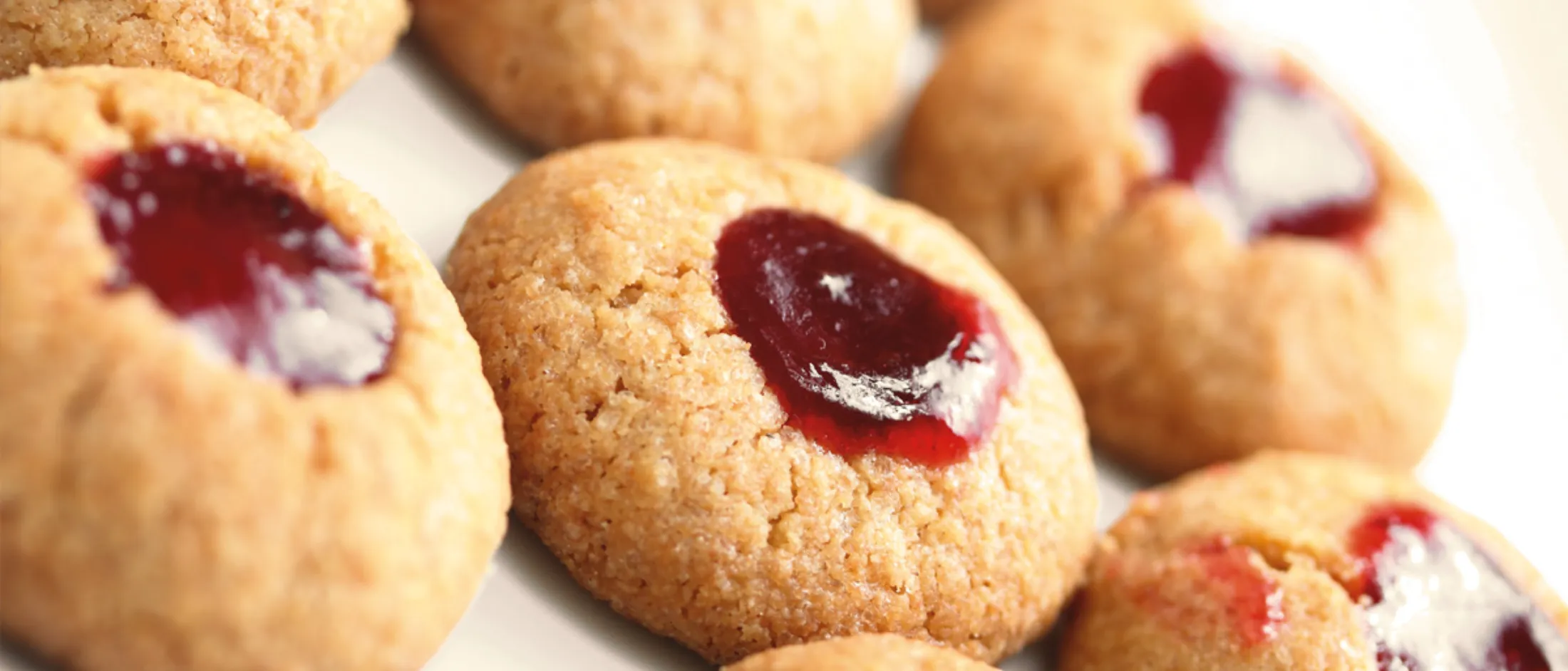 Nahaufnahme von Engelsaugen-Plätzchen mit roter Marmelade auf weißem Untergrund.