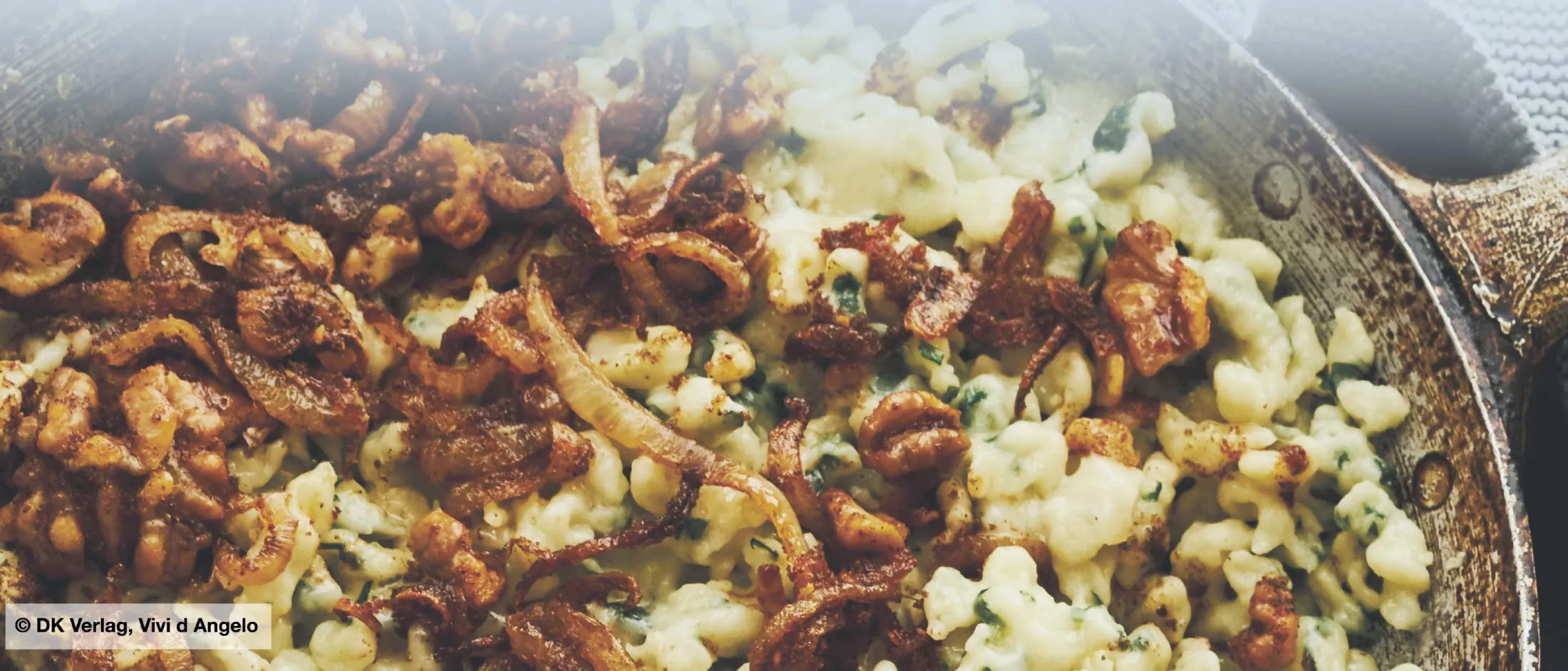 Pfanne mit Spinatspätzle und gebratenen Zwiebeln auf grauem Untergrund