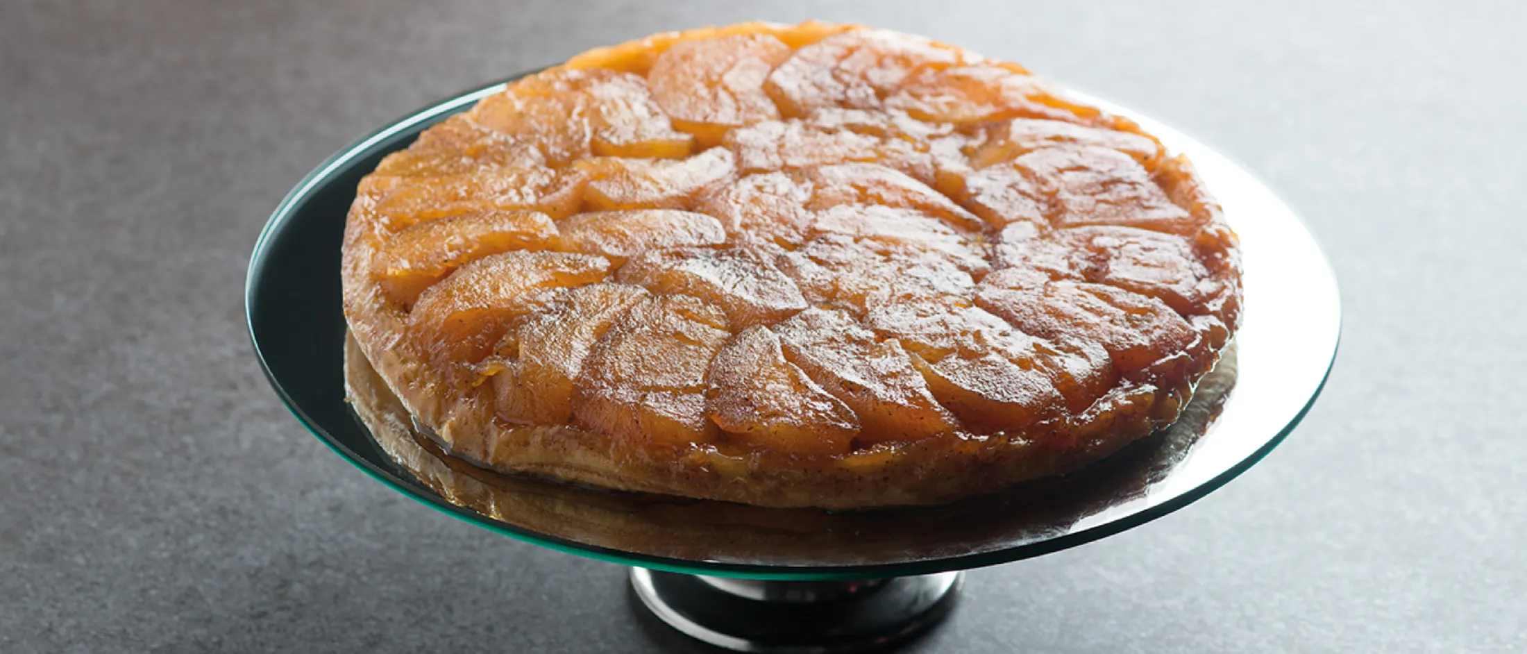 Torta di mele caramellate capovolta (tarte Tatin) su un'alzata di vetro.