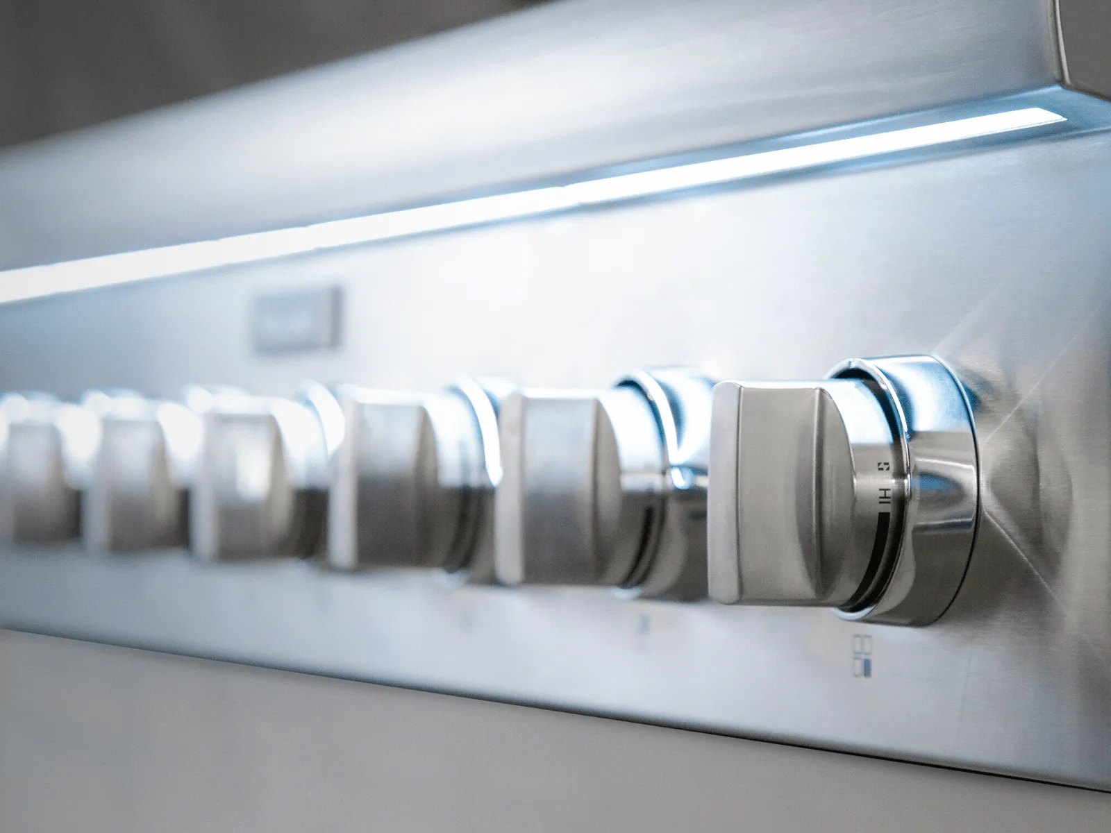 Close-up of stainless-steel range control knobs lined up under cool blue backlighting.