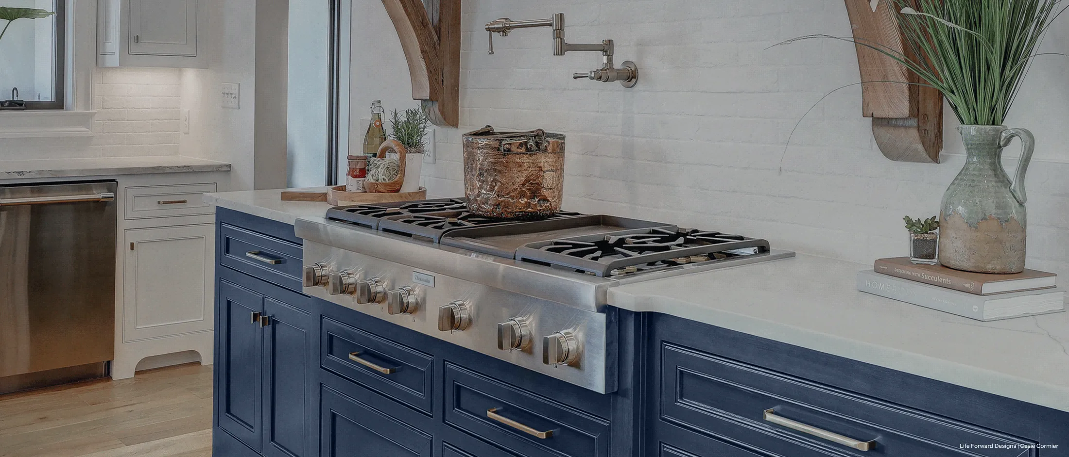 Modern kitchen featuring a sleek gas stove with stainless steel knobs, set in a blue island with white countertops and white brick backsplash.