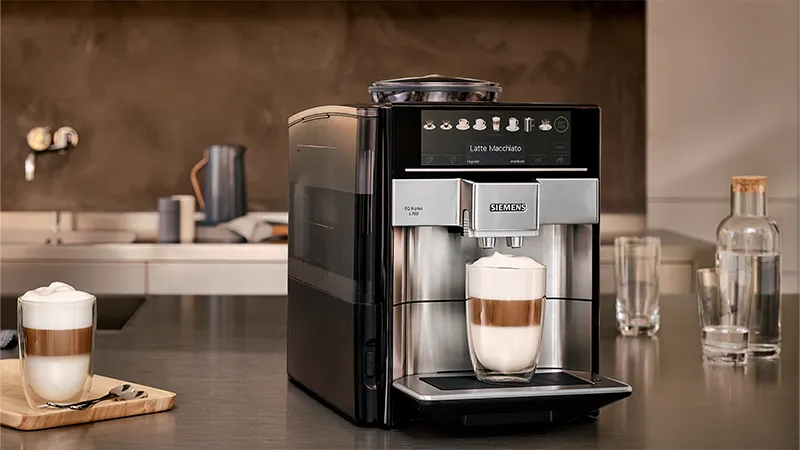 Sleek black coffee machine with Siemens branding, displaying a latte macchiato option, surrounded by coffee accessories.
