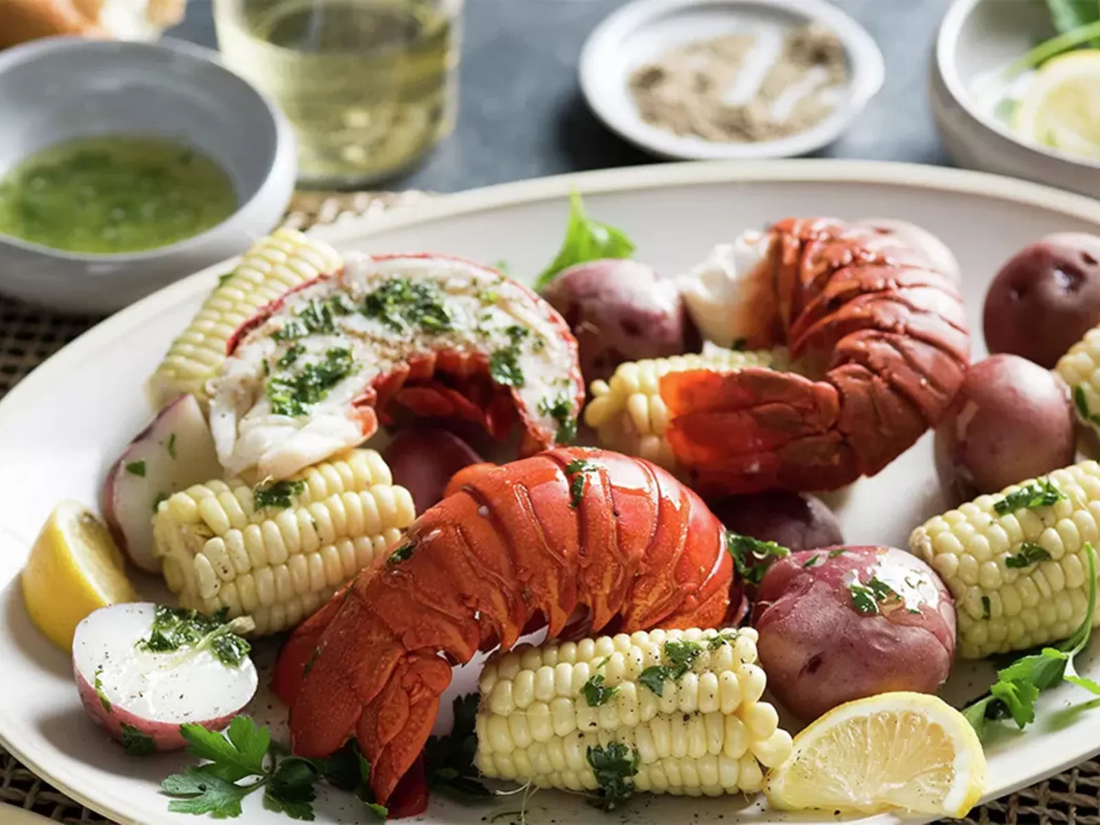 Lobster with corn on the cob, red potatoes, and lemon wedges on a platter.