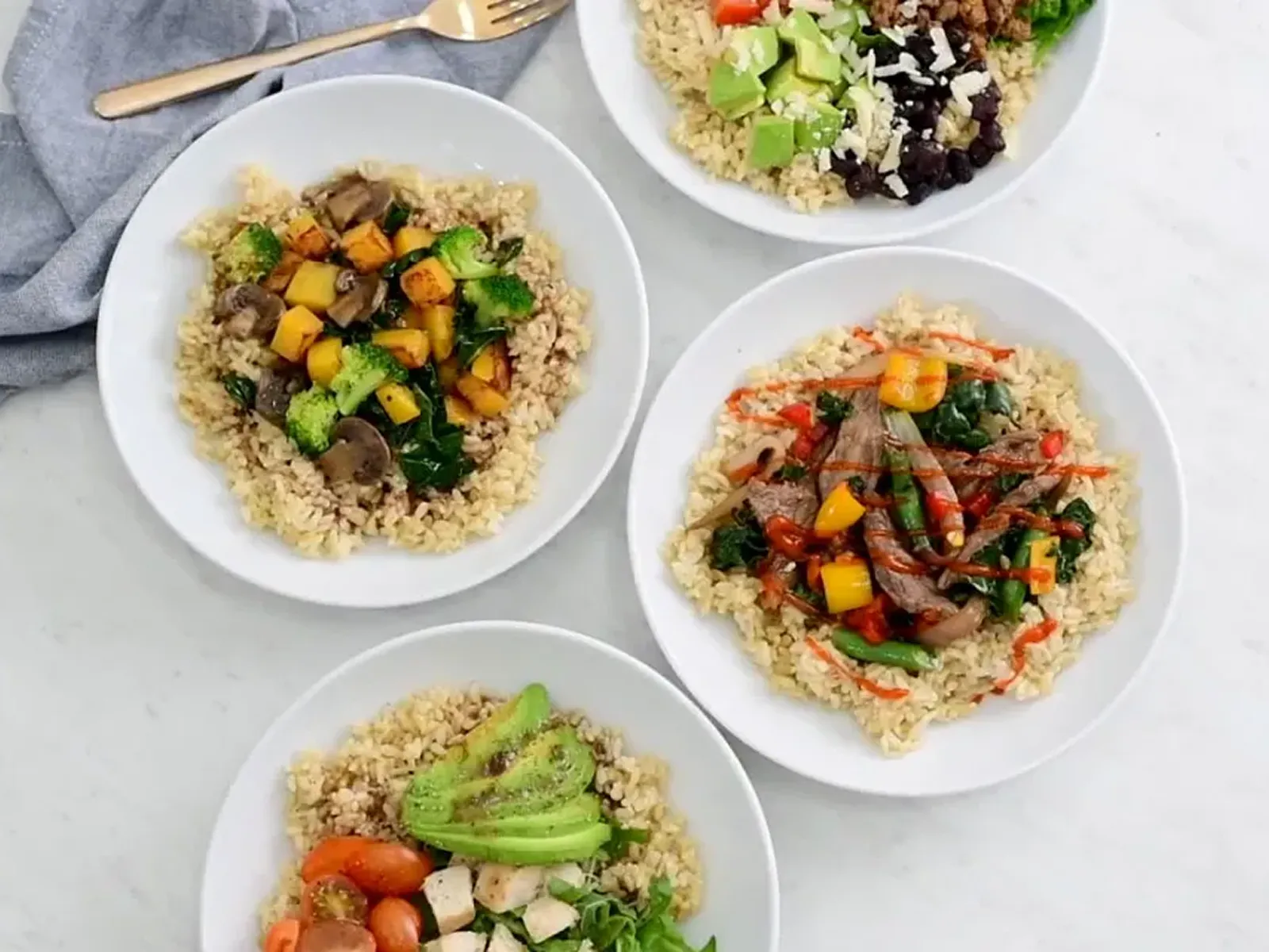Four healthy grain bowls with various toppings, seen from above.