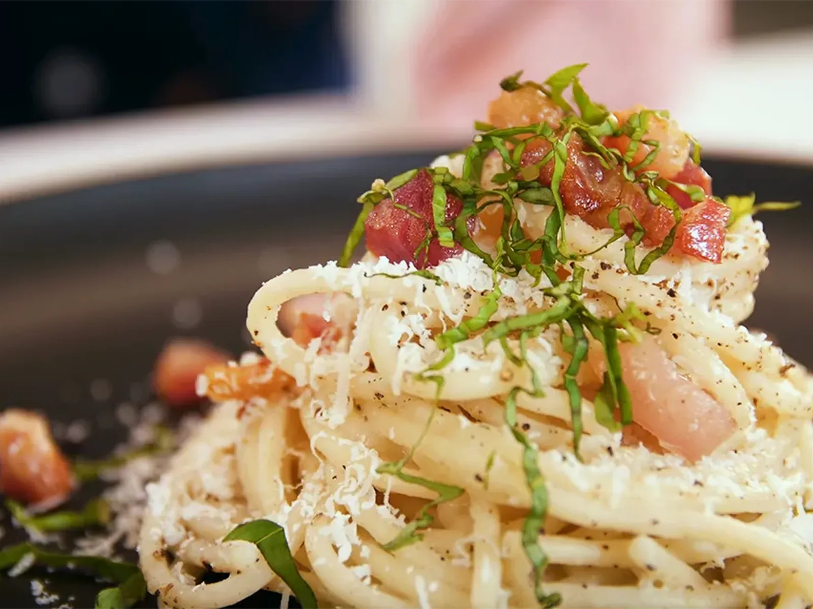 Close-up of pasta with bacon, grated cheese, and fresh herbs.