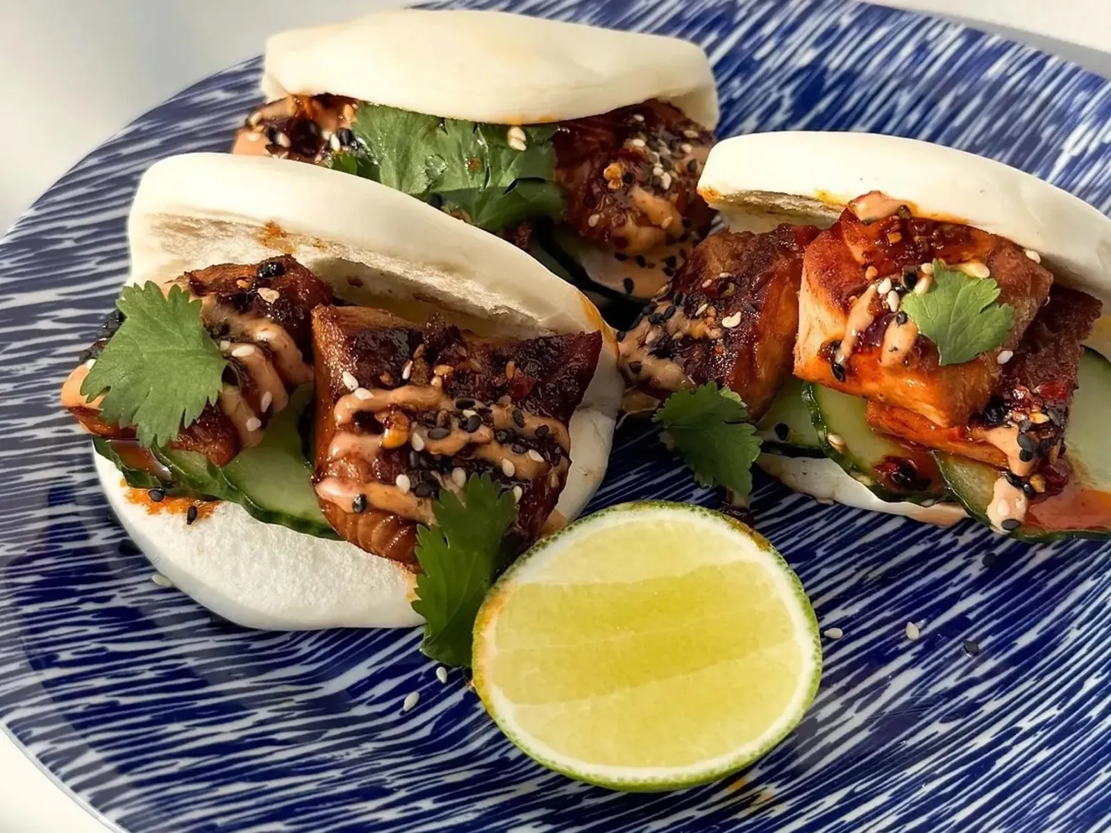 Pork belly bao buns with cucumber, cilantro, sauce, sesame, and lime.