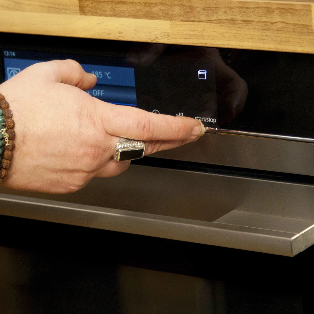 Una persona preme il pulsante di avvio su un forno moderno da incasso con display digitale, impostando la temperatura per la cottura.