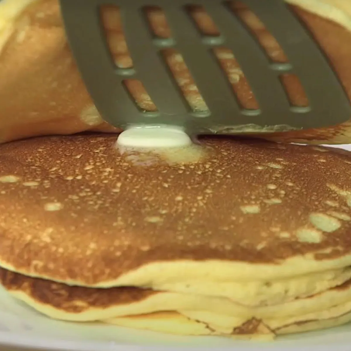 Pila di pancake su un piatto bianco con una spatola che solleva il pancake superiore