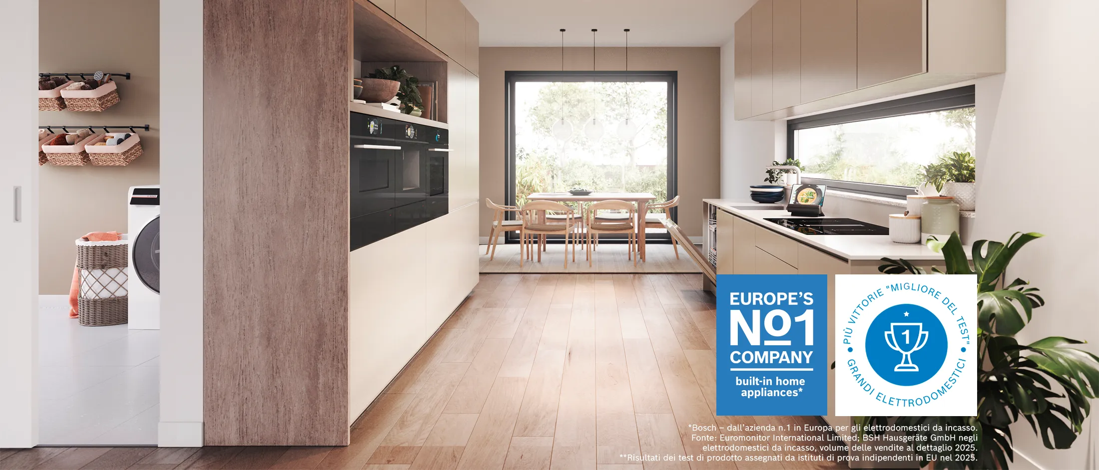 Cucina moderna con pavimento in legno chiaro, forni a muro, zona pranzo con ampia finestra e zona lavanderia con cestini e lavatrice.