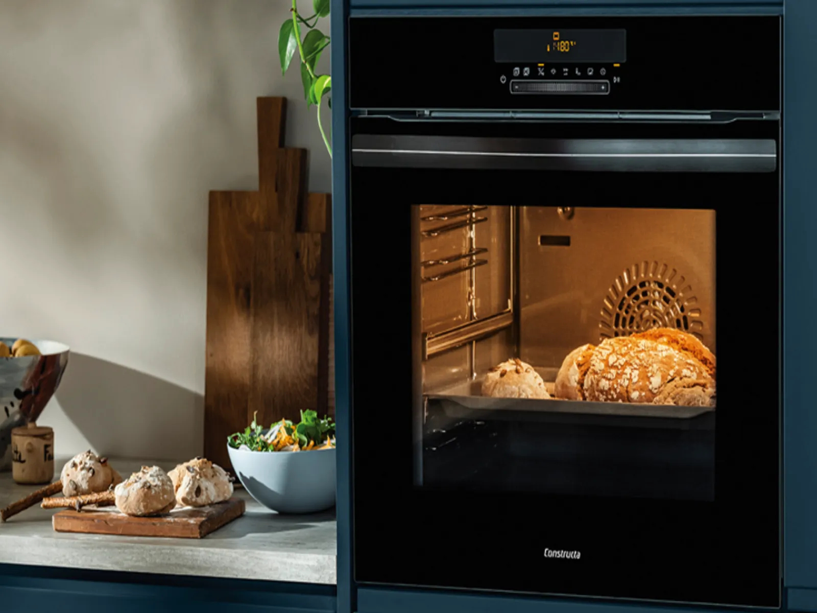 Backofen mit zwei Broten im Inneren und Küchenarbeitsfläche mit Schüssel, Schneidebrett und Brotlaiben daneben