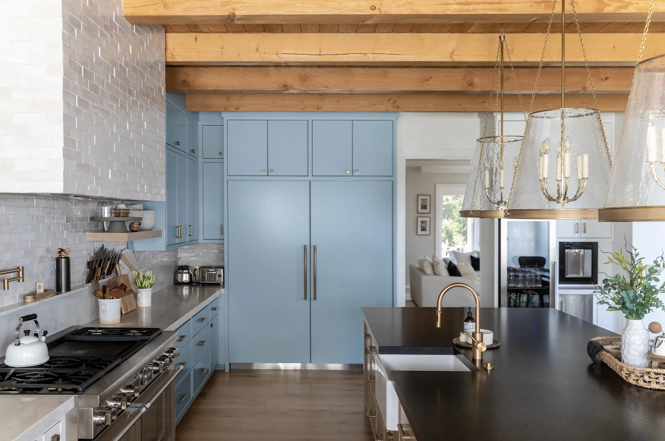 Modern kitchen with light blue cabinets, wooden beam ceiling, large island with black countertop, and stainless steel appliances.