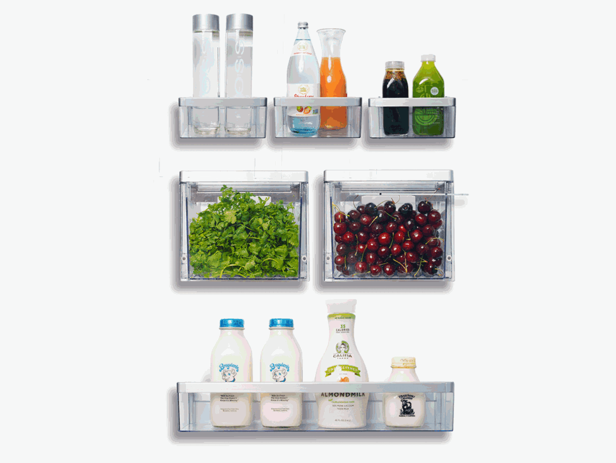 Clear refrigerator storage bins organized with bottles, leafy greens, cherries, and dairy products against a white background.