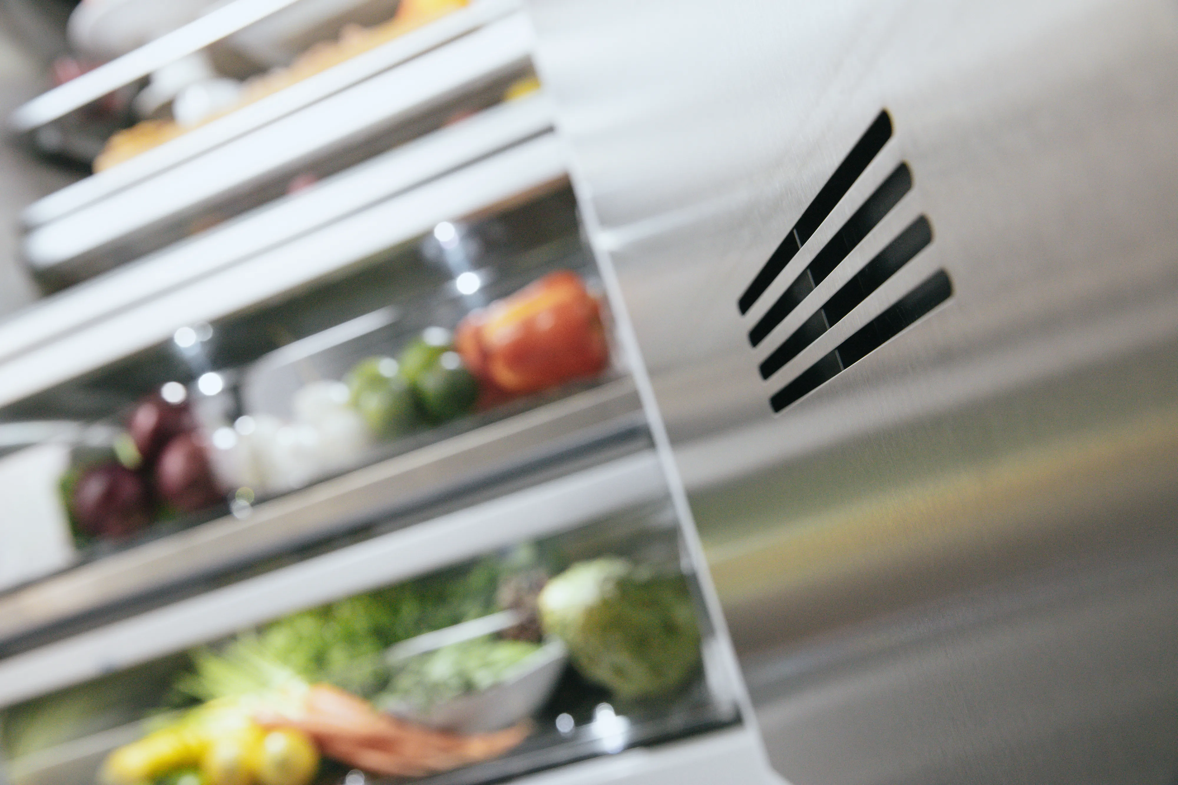 Open refrigerator door showing fresh vegetables and eggs on shelves inside a stainless steel fridge.