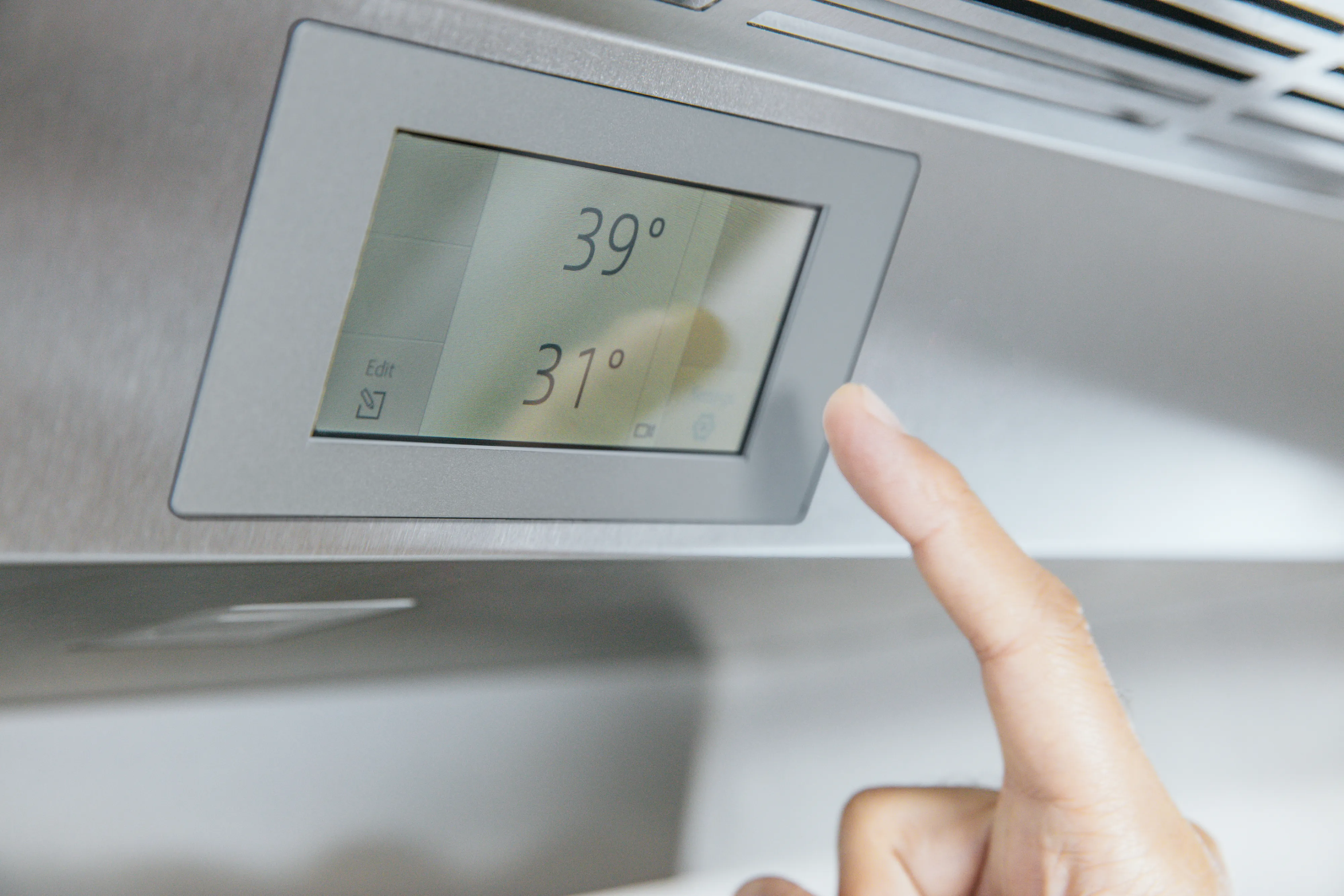Close-up of a hand adjusting a digital thermostat displaying temperatures of 39° and 31°.