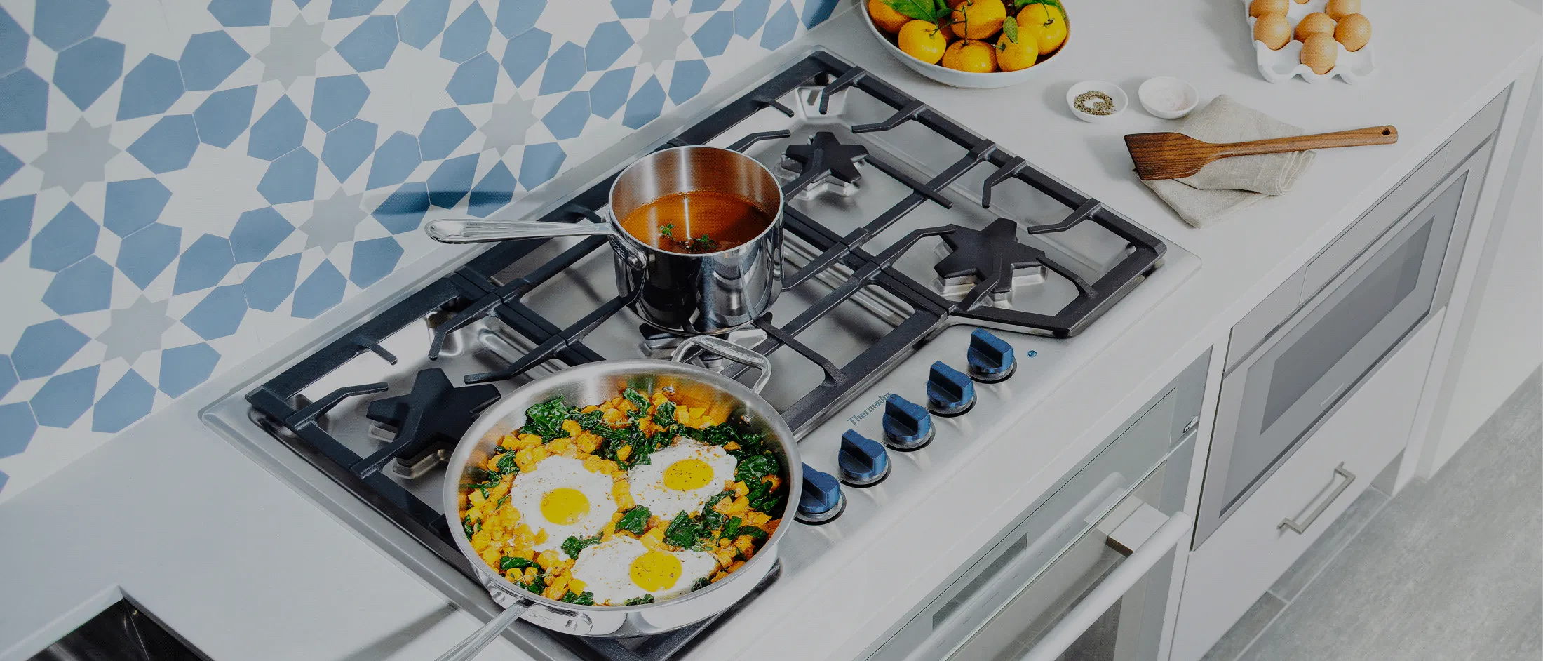 A gas stove with two pans cooking, one with soup, another with eggs and greens.