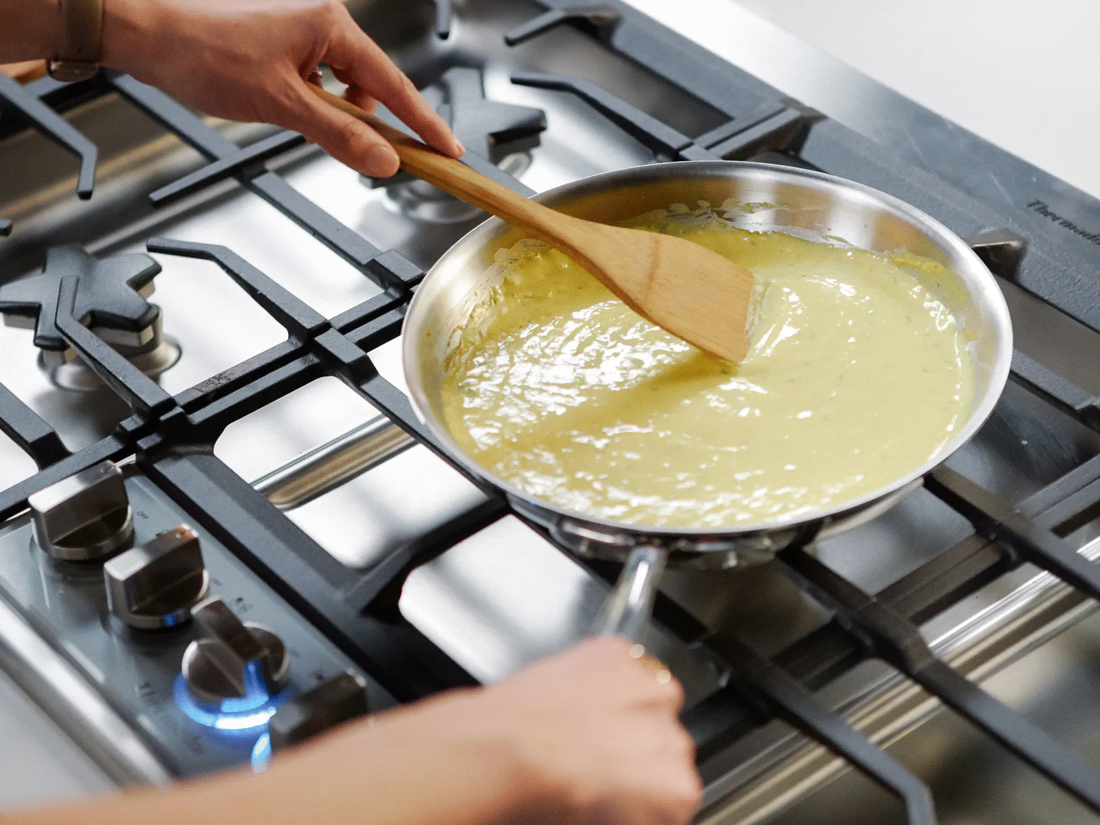 Person stirring eggs in a pan on a gas stovetop.