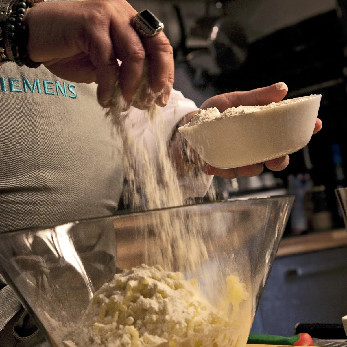 Mani cospargere di farina su purè di patate in una ciotola di vetro; cuoco che indossa un grembiule Siemens
