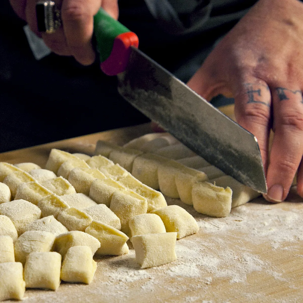 Mani affettare gnocchi corde in pezzi su una tavola di legno infarinato