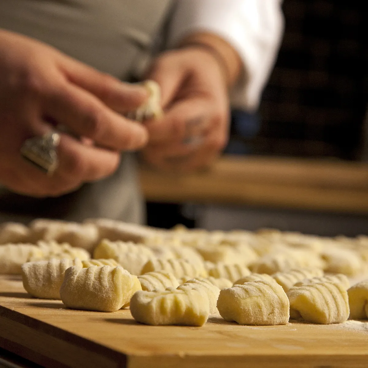 Gnocchi di patate infarinati su una tavola di legno, mano che modella uno sullo sfondo sfocato