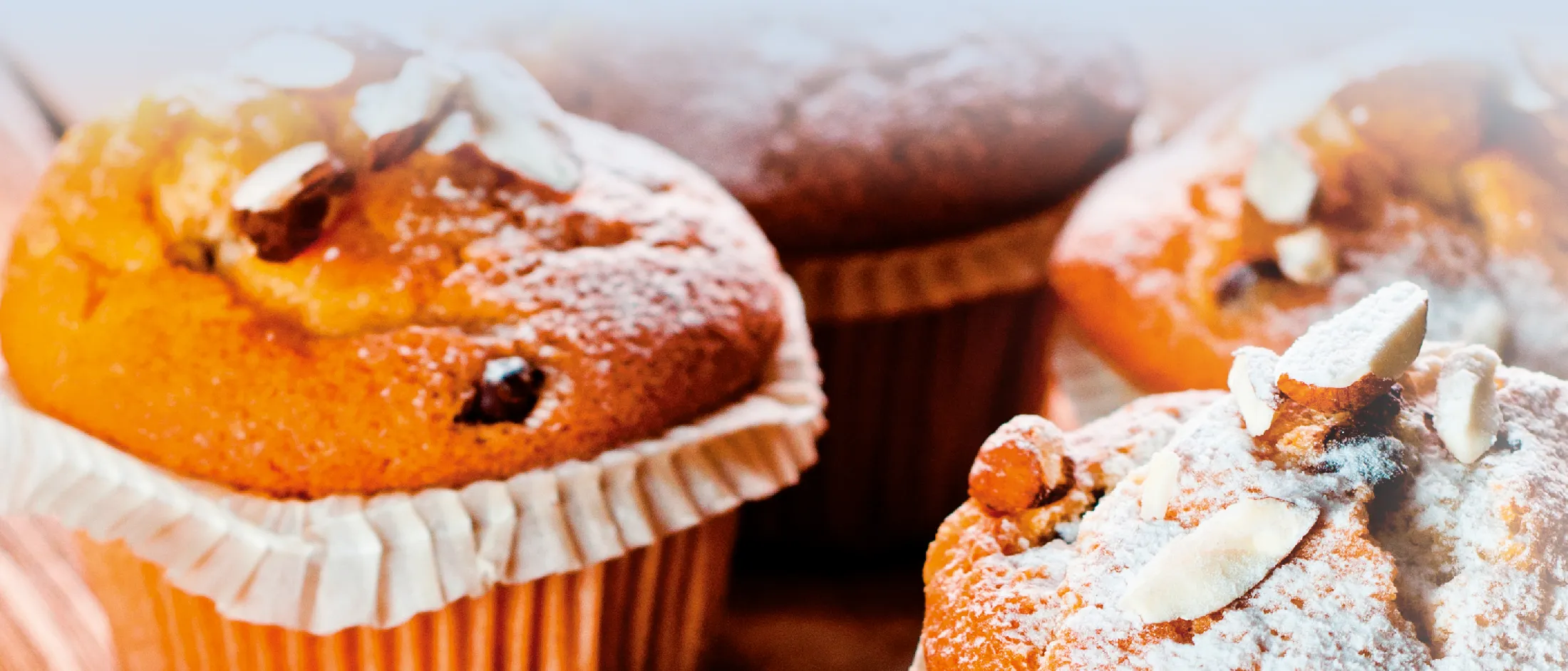 Nahaufnahme von frisch gebackenen Muffins, bestreut mit Puderzucker und Mandelsplittern.