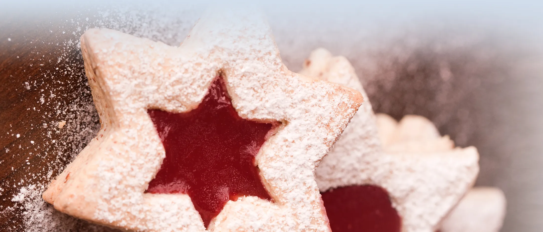 Sternförmige, mit Marmelade gefüllte Kekse, mit Puderzucker bestäubt, auf einer Holzoberfläche.