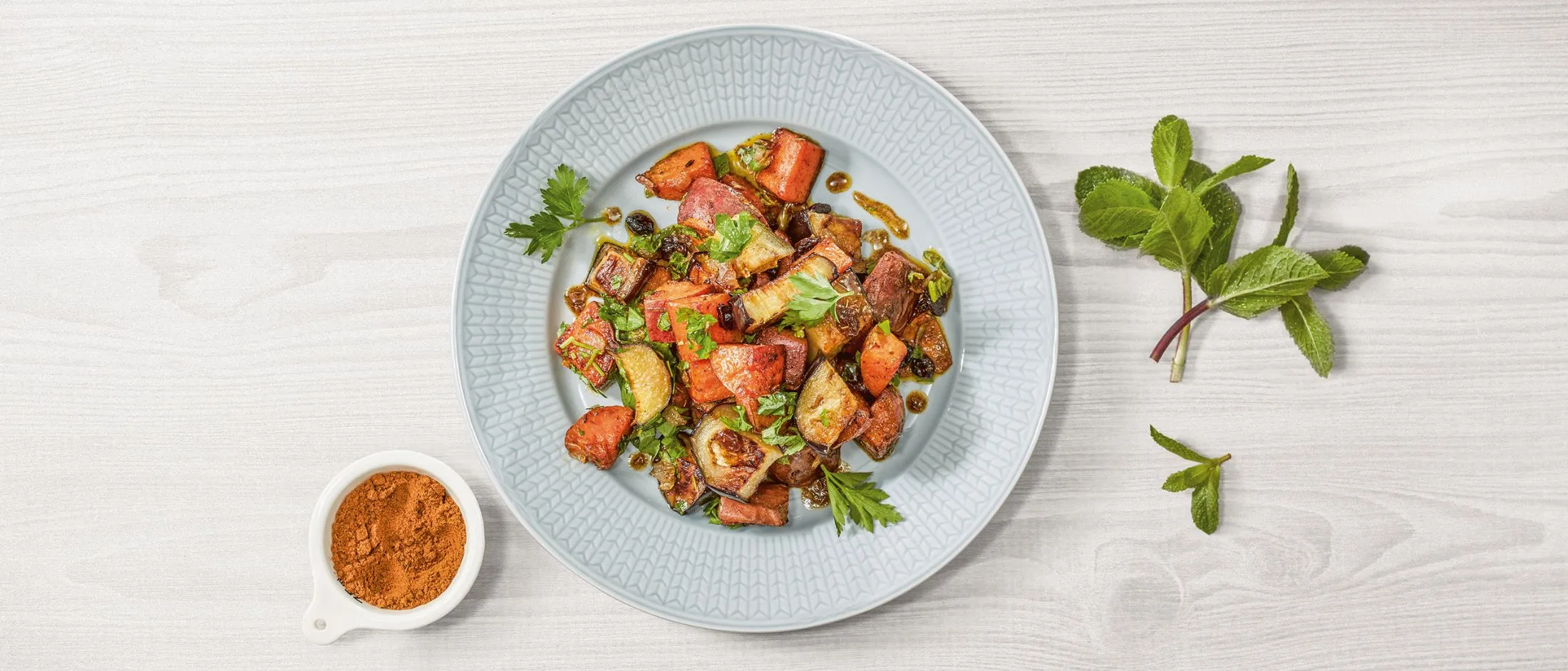Piatto di verdure arrosto, tra cui patate, pomodori e erbe, con un contorno di spezie.