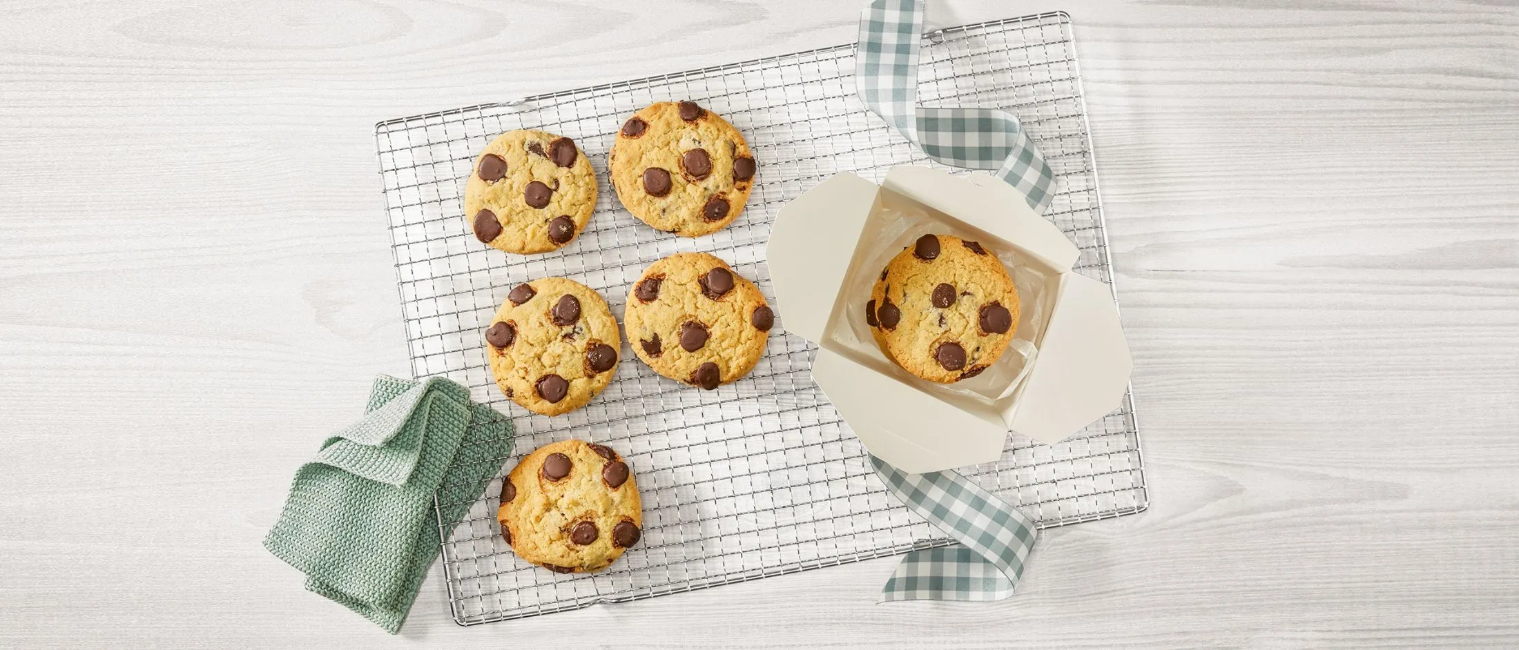 I biscotti di cioccolato appena sfornati su un rack di raffreddamento, con una scatola e un asciugamano da cucina.
