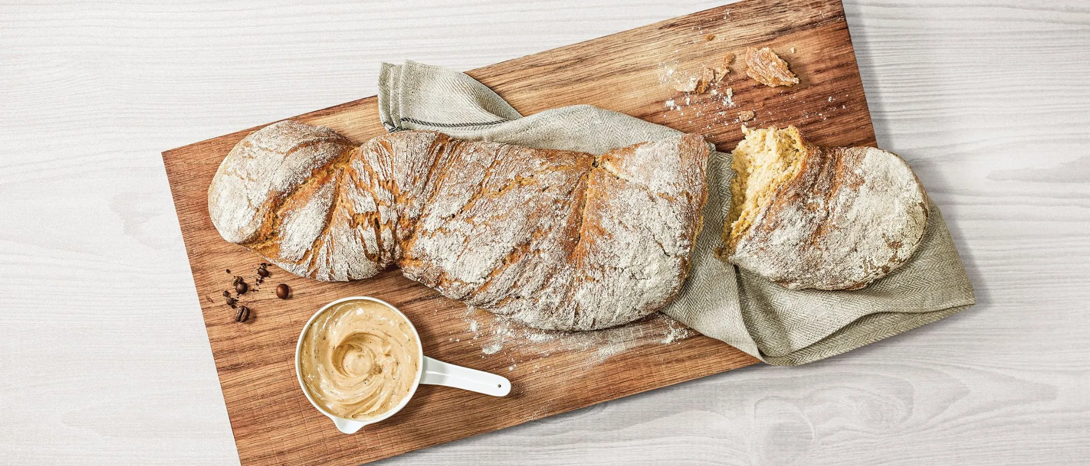 Pane artigianale appena sfornato, burro e tavola di legno su fondo bianco.