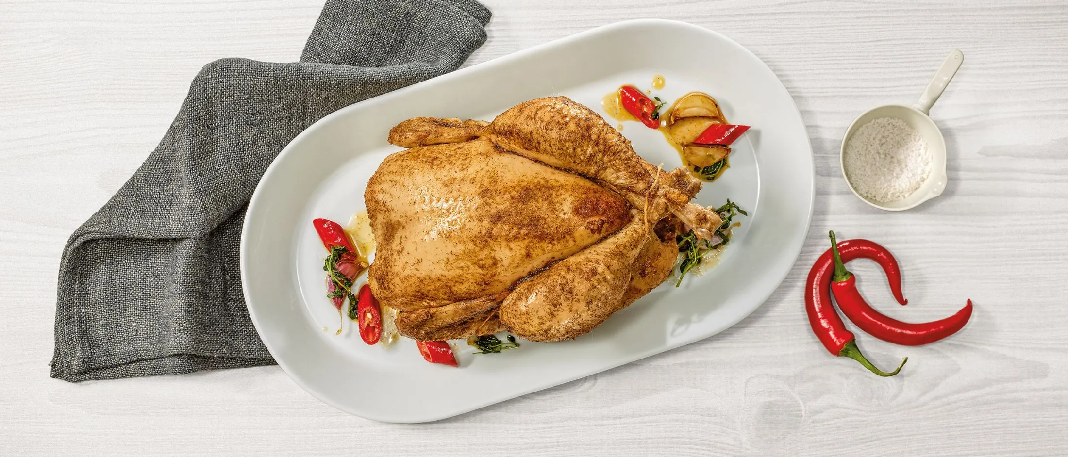 Pollo arrosto con verdure su un piatto bianco, accompagnato da un tovagliolo grigio e peperoncino.