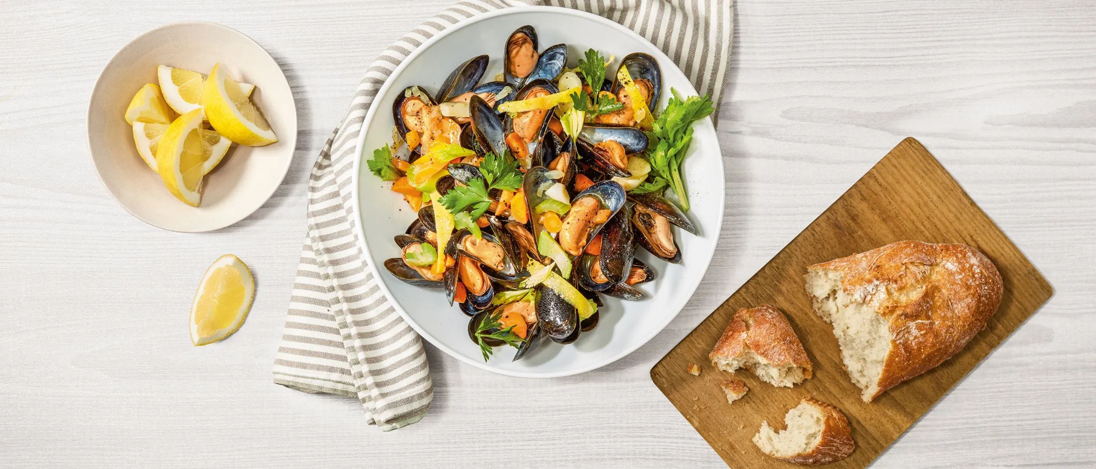 Piatto di frutti di mare con cozze, pane e fette di limone su un tavolo di legno.