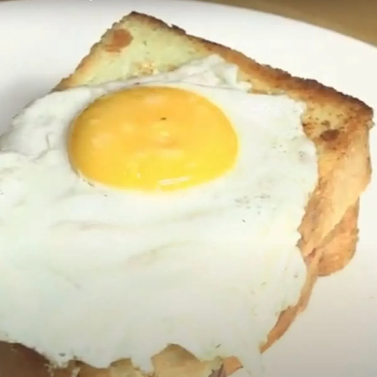 Uovo fritto su una fetta di pane tostato su un piatto bianco.