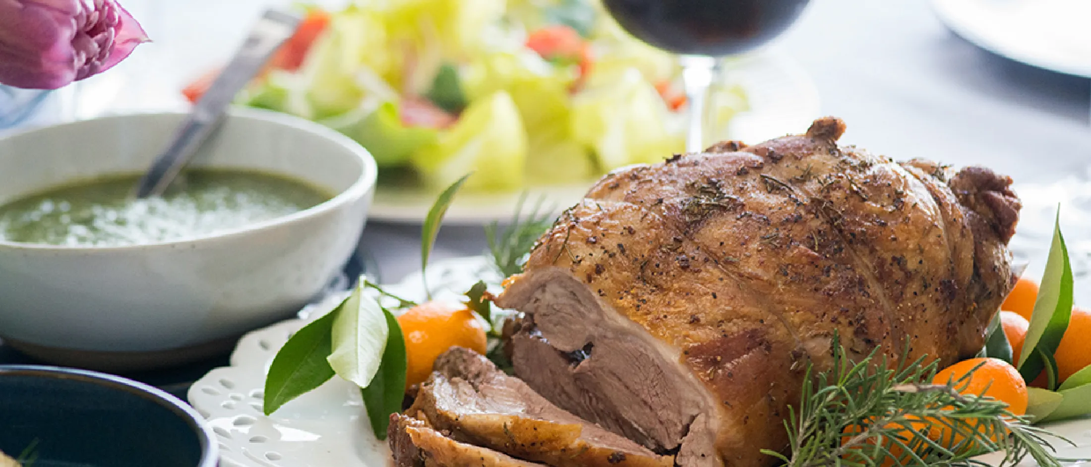 Roasted turkey, salad, soup, wine, and flowers on a table - a festive holiday meal